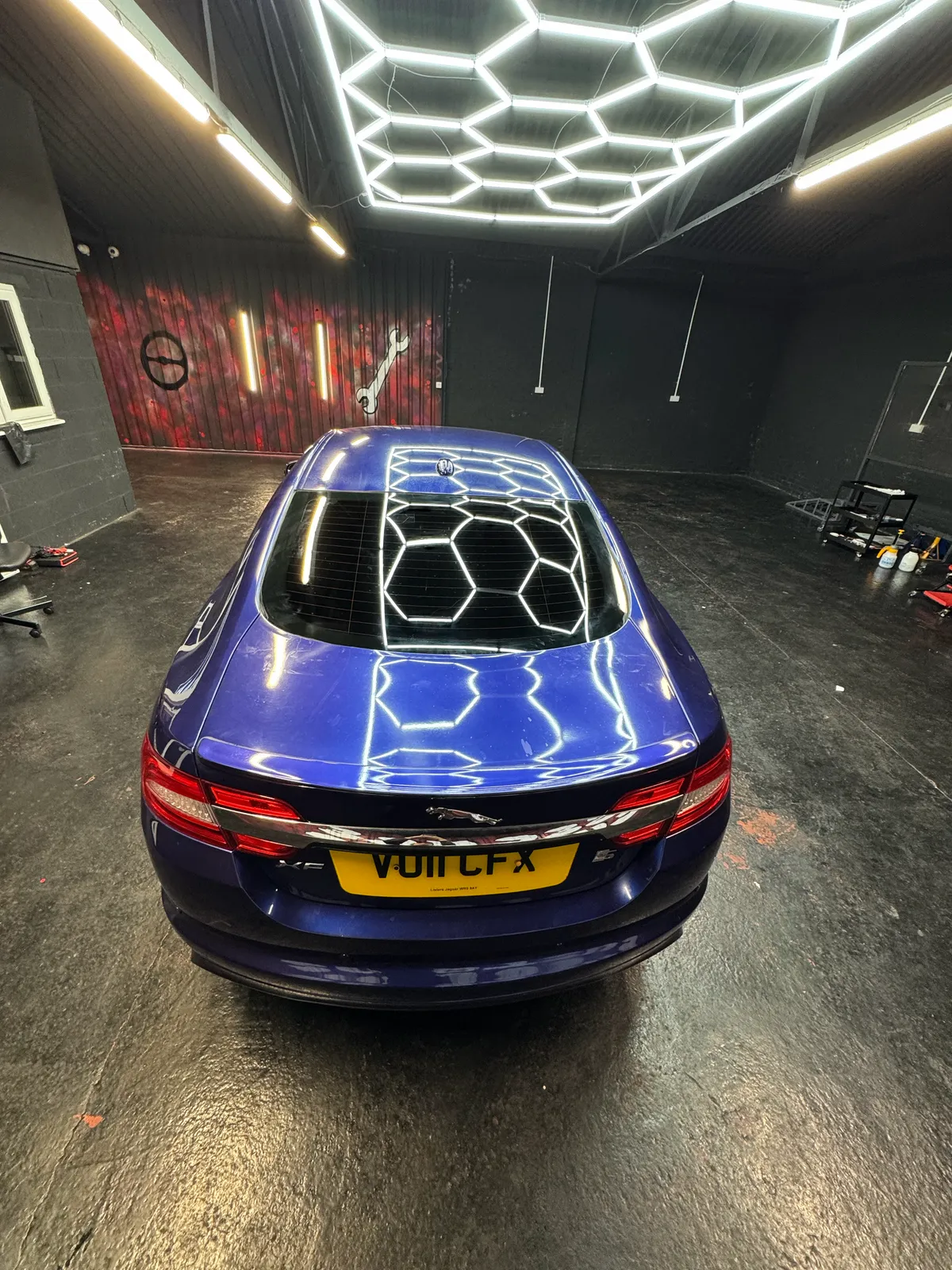 Blue Jaguar XF with a tinted rear windscreen under the Secure Customs hexagon lighting.